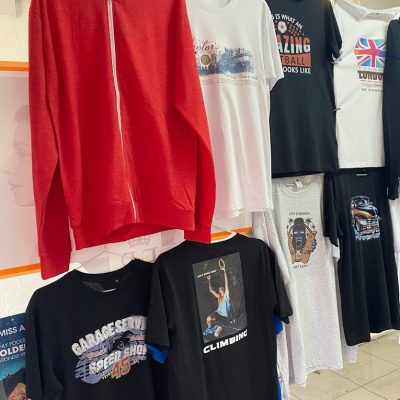 Clothing rack displaying printed T-shirts in various colors including red, white, and black.