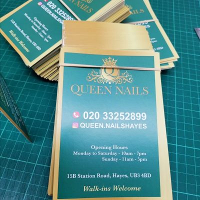 Stack of teal and gold business cards reading “Queen Nails” with contact number “020 33252899” and address details.