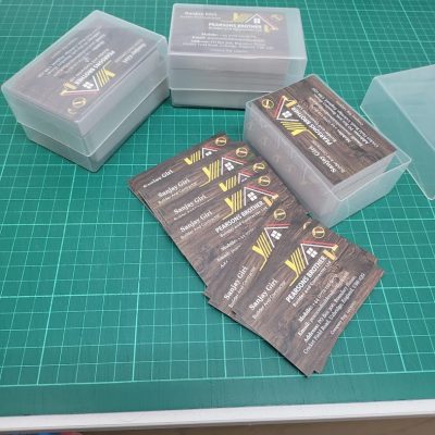 Small plastic boxes and a stack of printed business cards placed on a green cutting mat.