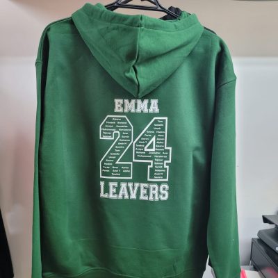 Green hoodie hanging on a rack with white text “EMMA 24 LEAVERS” printed on the back.